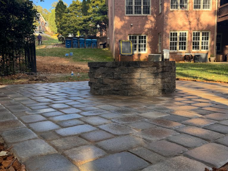 custom paver patio with stone fire pit in charlotte nc, surrounded by wooded landscape for outdoor relaxation and entertaining