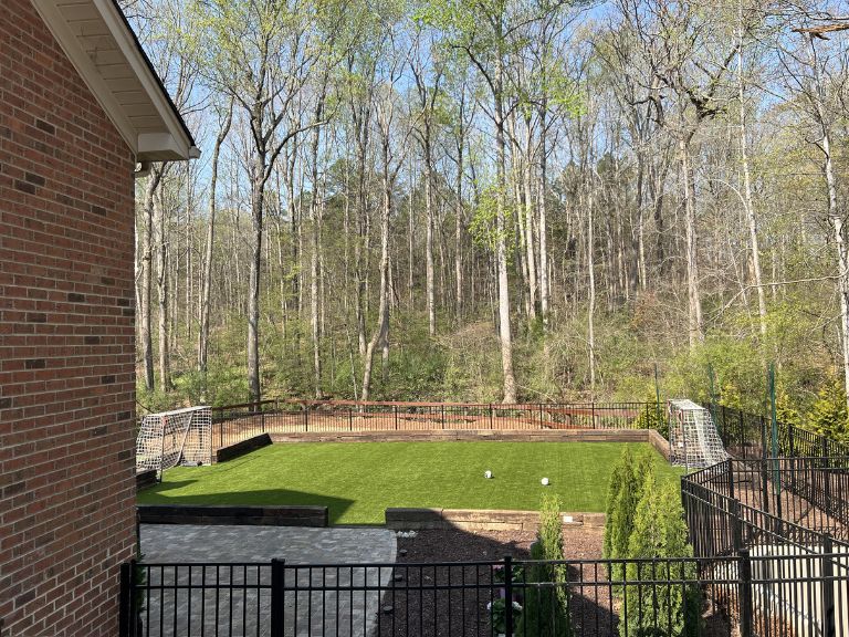 Backyard perimeter edge of artificial turf installation at Carmel Commons Fort Mill SC showing clean fence border by CLT Pros