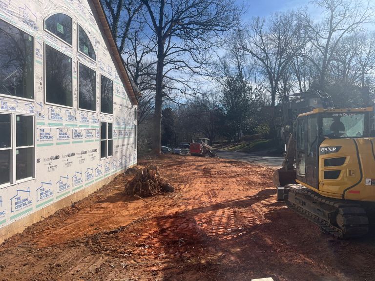 excavator grading cleared soil beside home foundation in matthews, nc