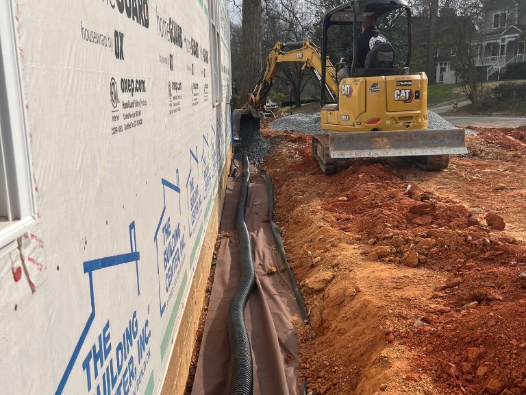 excavator installing corrugated drain pipe along foundation trench in matthews, nc