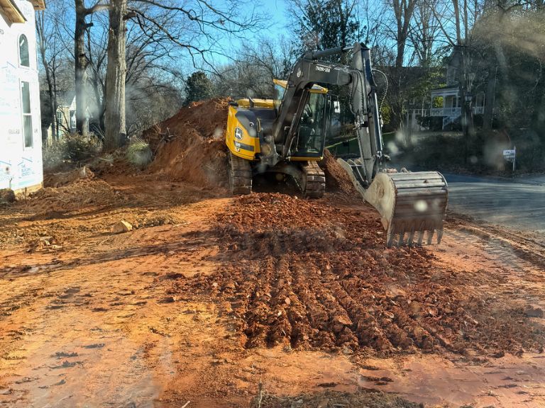 excavator tilling and leveling soil pile during grading job in matthews, nc