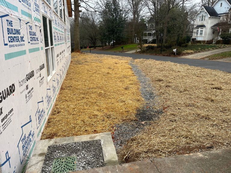 graded side yard with straw cover and gravel drainage channel to foundation drain in matthews, nc