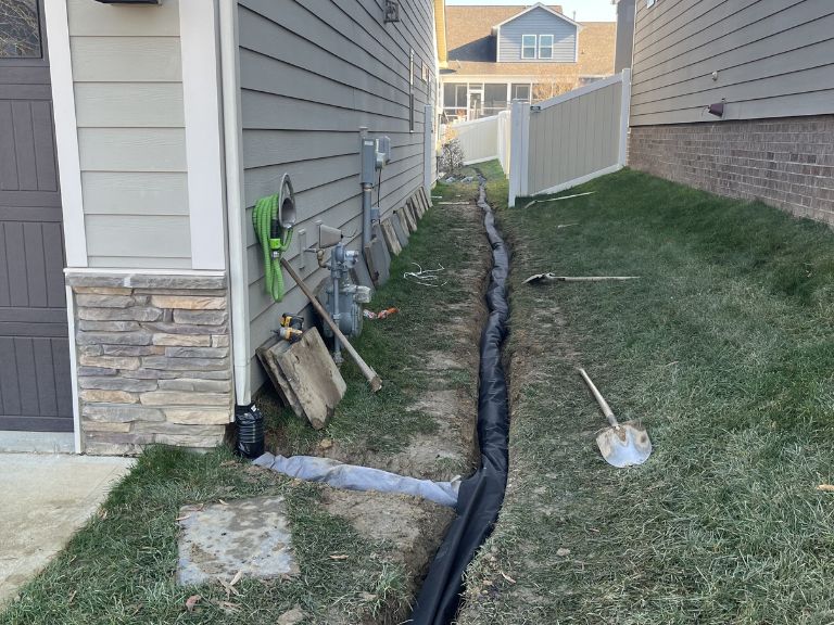 perforated drain pipe being laid in trench during french drain installation in huntersville, nc