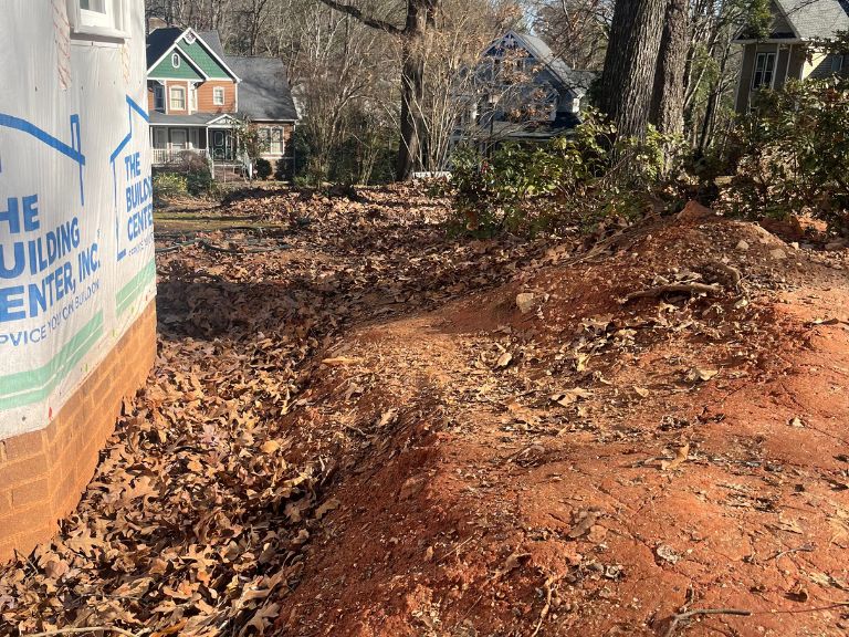 leaf-covered yard and dirt mound beside home foundation before grading in matthews, nc