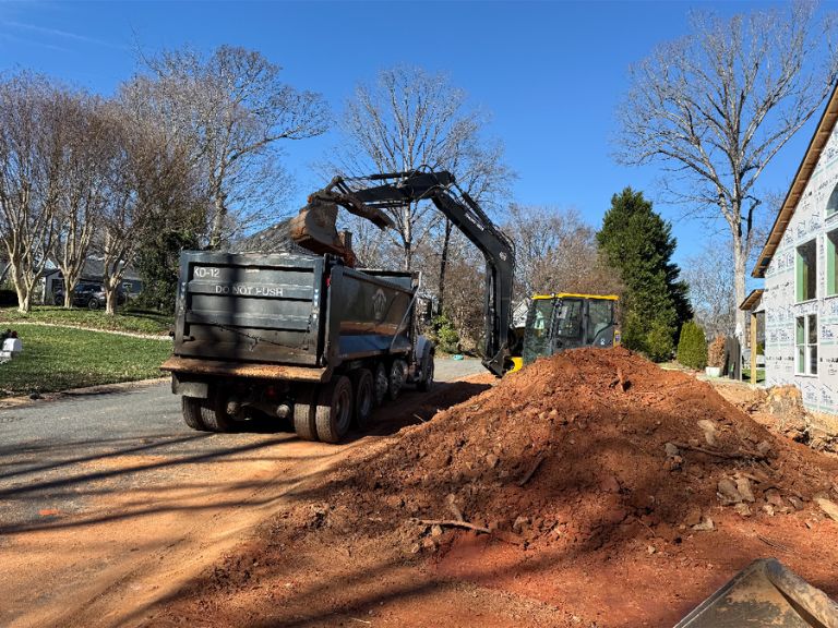 excavator loading dump truck with excess dirt during grading job in matthews, nc
