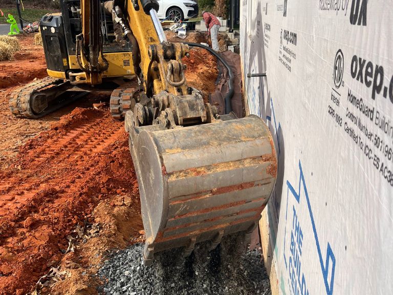 mini excavator digging gravel trench along foundation wall in matthews, nc by clt pros