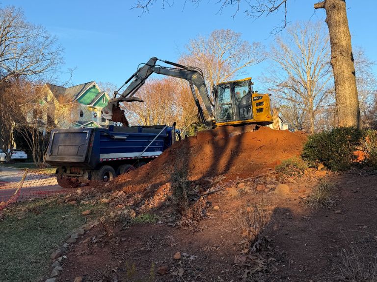 excavator loading dirt pile into dump truck during yard grading in matthews, nc
