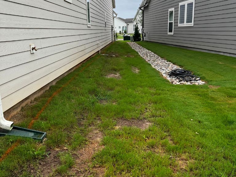 patchy bermuda grass side yard with rock drainage channel along home foundation before sod replacement in waxhaw nc — clt pros
