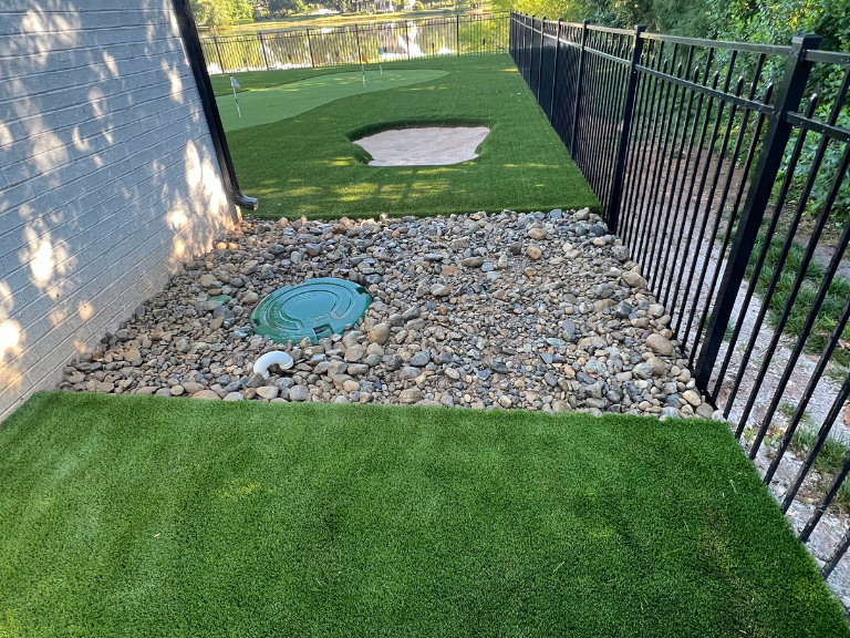 river rock drainage bed with a drain inlet beside new artificial turf in weddington, nc