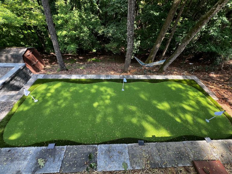 overhead view of completed artificial turf putting green with three flags surrounded by paver coping and wooded lot in tega cay sc — clt pros