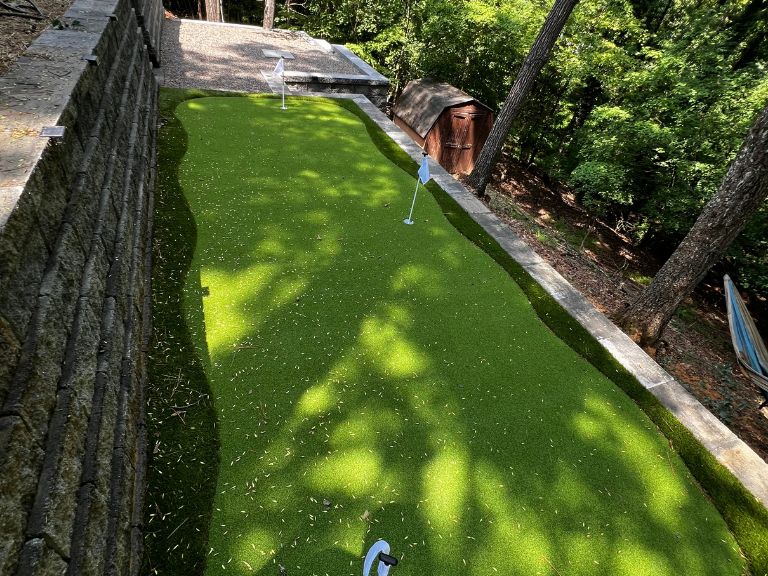 side-angle view of artificial turf putting green against terraced granite retaining wall in wooded tega cay sc backyard — clt pros