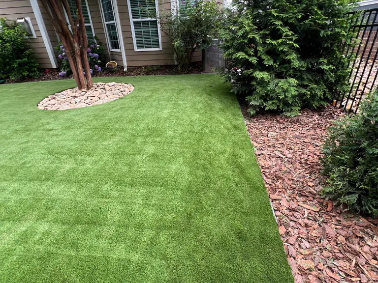 new artificial turf lawn with a river rock tree ring and mulch bed beside the house in tega cay, sc