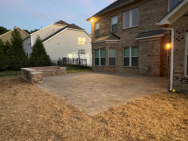 new paver patio with a stone seating wall and pine straw border at dusk in weddington, nc