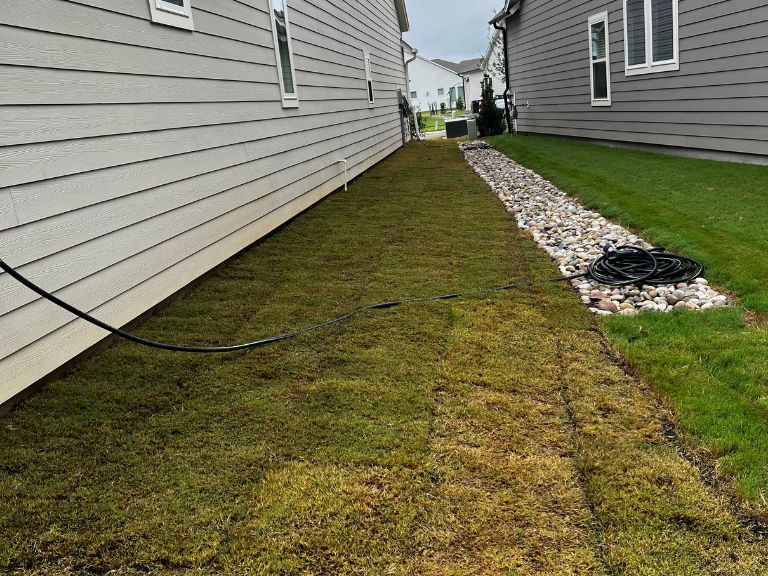 patchy bermuda grass side yard with river rock drainage channel and grass dying off near home foundation in waxhaw nc