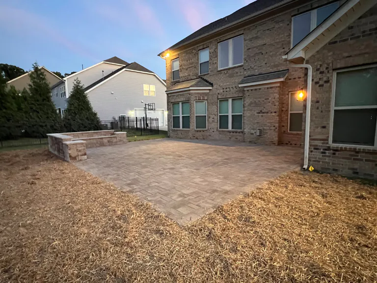 paver patio and seating wall behind a brick home with the porch light on in weddington, nc