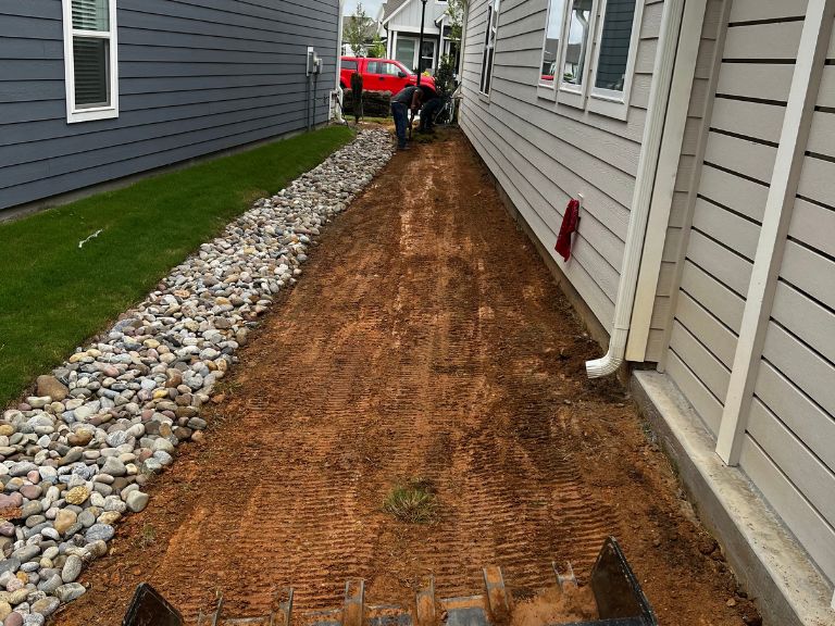 cleared side yard with red clay soil exposed and river rock drainage channel after bermuda grass removal in waxhaw nc — clt pros