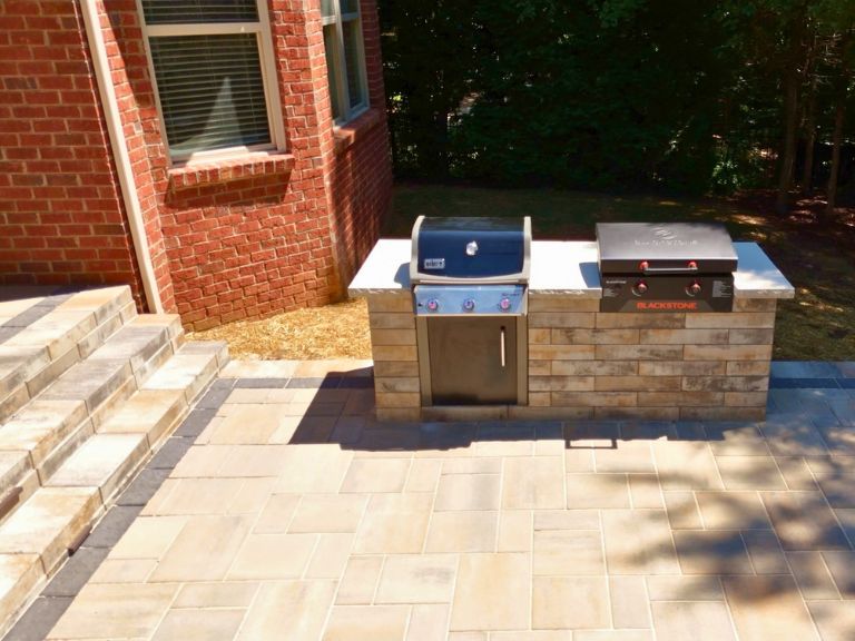 built-in grill island with stone countertop, gas grill, and griddle on a paver patio in indian land, sc