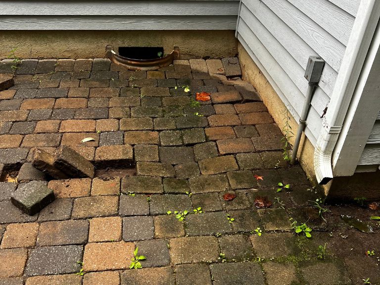 loose and settled pavers at the downspout corner of the house before patio replacement in huntersville, nc