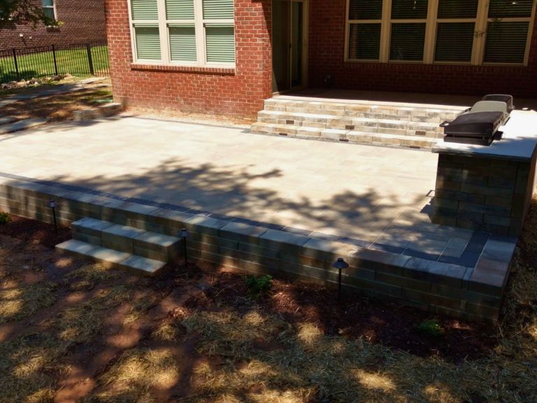 elevated view of a raised paver patio, curved retaining wall, and grill island behind a brick home in indian land, sc
