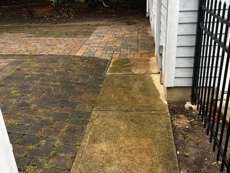 weed-filled paver patio meeting the concrete side walkway beside a black iron fence in huntersville, nc