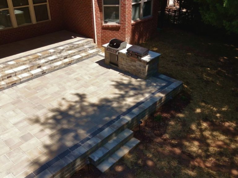 raised paver patio with grill island and retaining wall steps down to the yard in indian land, sc