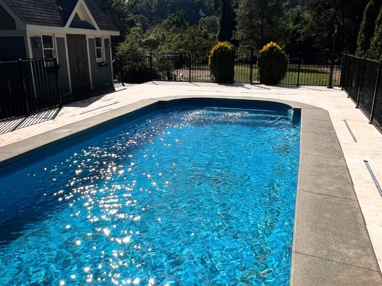 close view of pool coping and travertine deck in afternoon sun in grier heights, charlotte, nc
